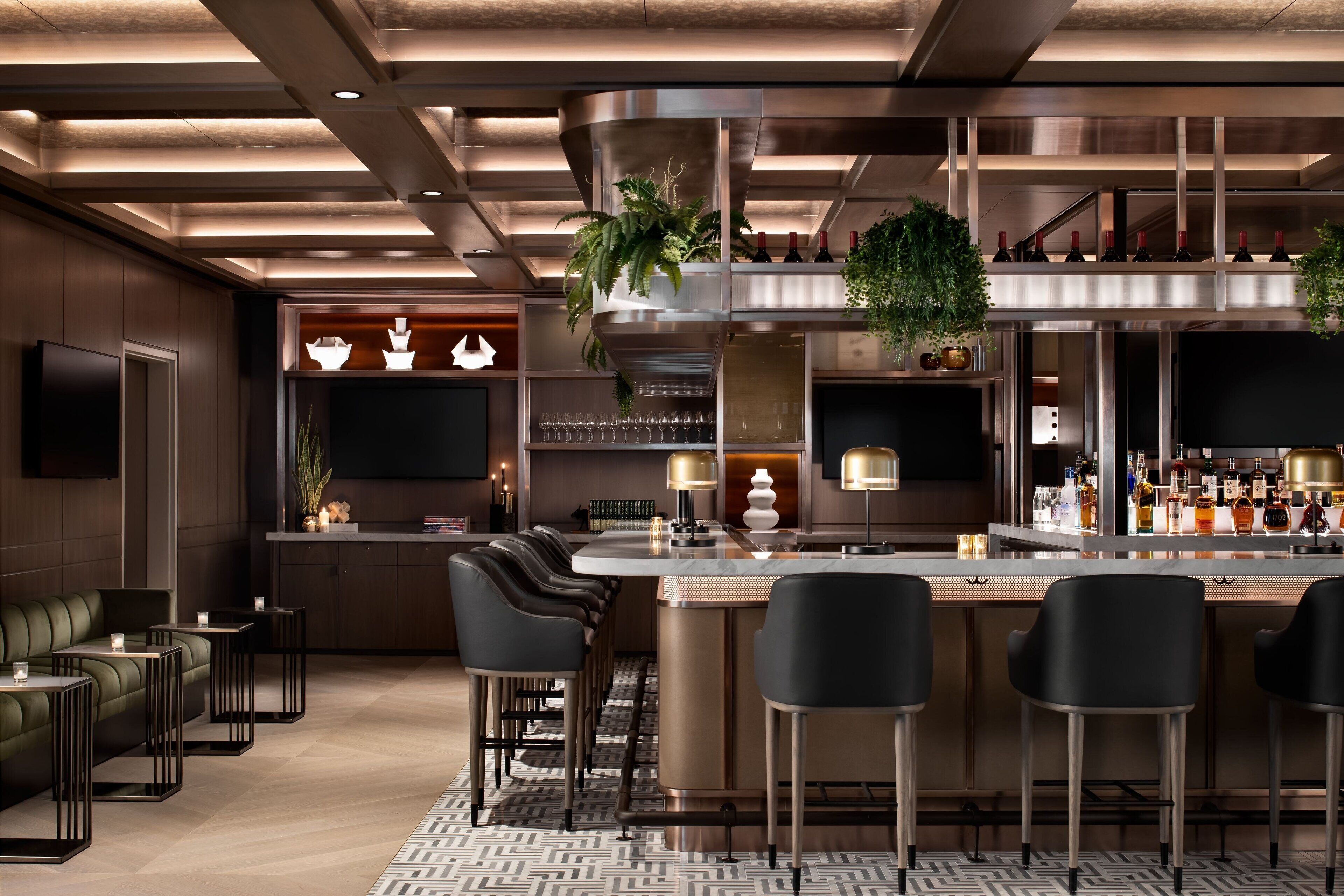 Zona de bar moderna con una isla central, taburetes y un área de estar con sofá y sillones.