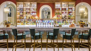 Uma área de bar com várias prateleiras de garrafas, um vaso decorativo central e banquetas de bar.