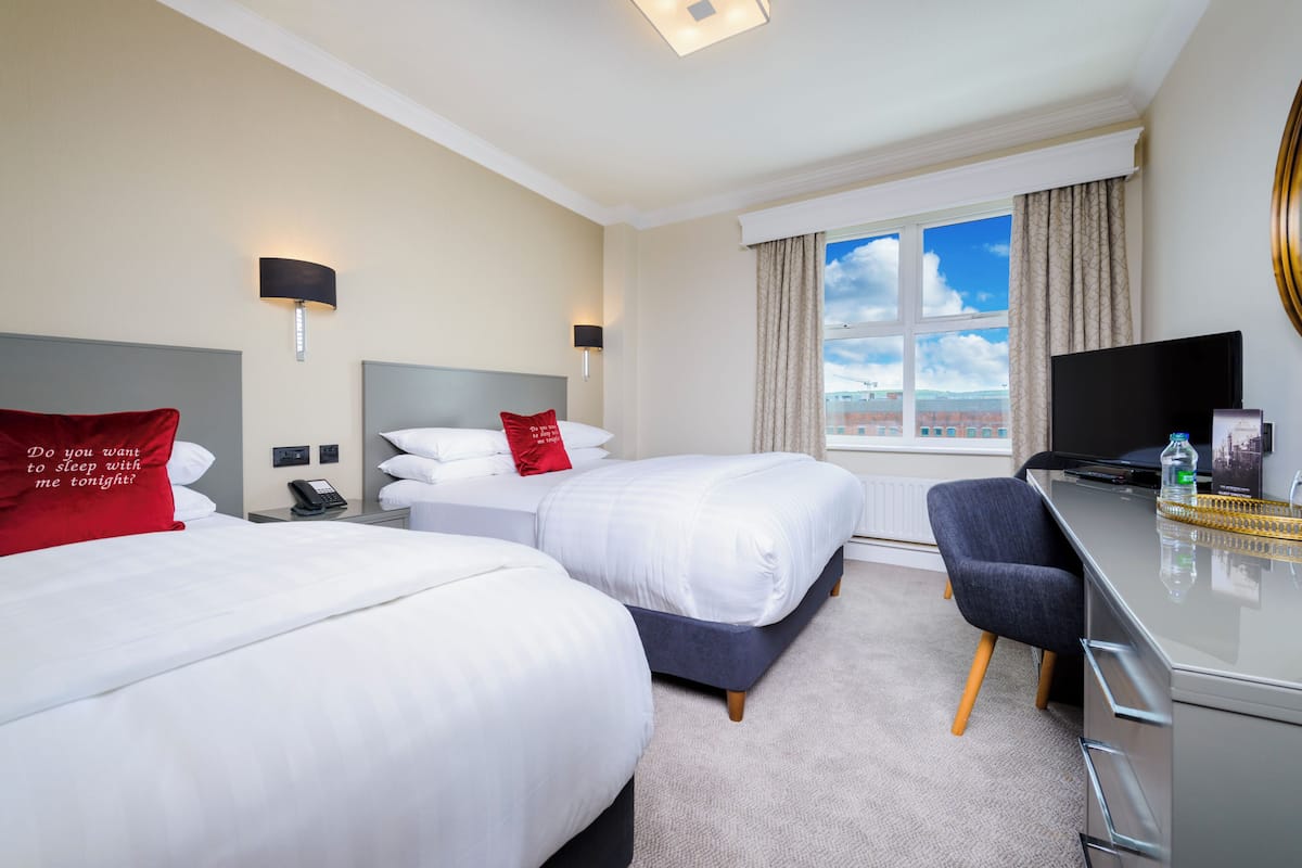 A hotel room with two beds, a desk, a chair, a TV, and a window with a view.