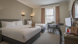 Quarto de hotel com duas camas, uma escrivaninha, uma cadeira, uma televisão e uma janela com cortinas.