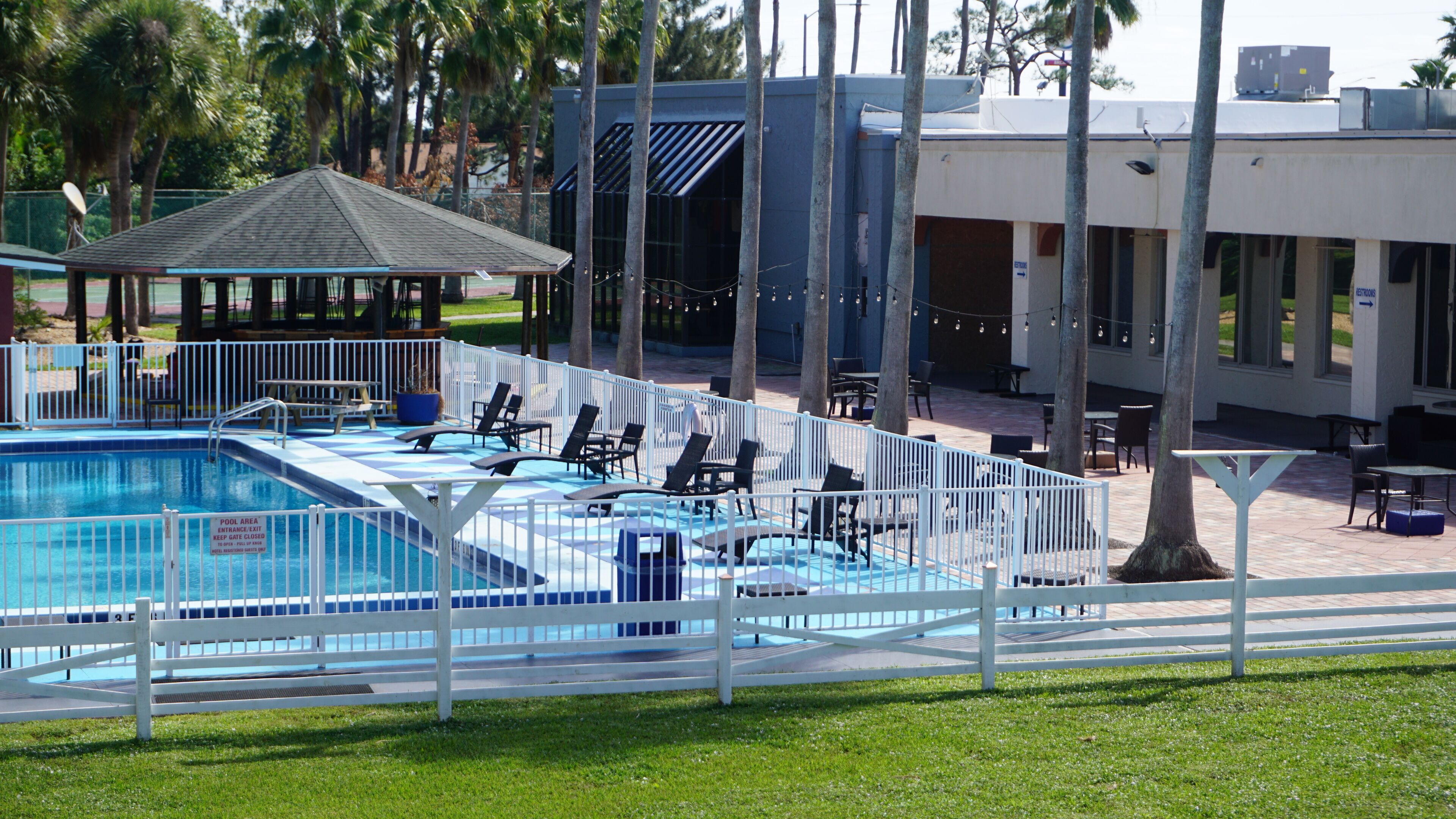 A pool area with lounge chairs and a gazebo, surrounded by a white fence.