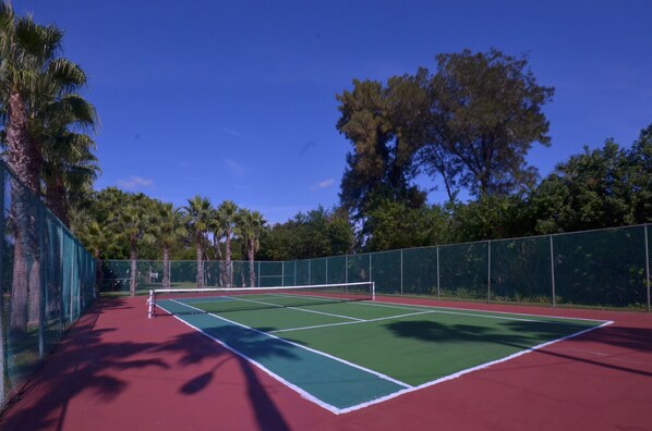 A tennis court with a net, surrounded by a green fence and palm trees. - Island Hotel of the Space Coast (Merritt Island)