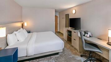 Habitación de hotel con cama, escritorio, silla, televisor y una pequeña kitchenette.