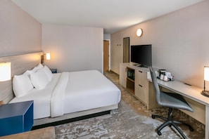 Habitación de hotel con cama, escritorio, silla, televisor y una pequeña kitchenette.
