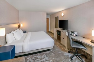 A hotel room with a bed, desk, chair, television, and a small kitchenette.
