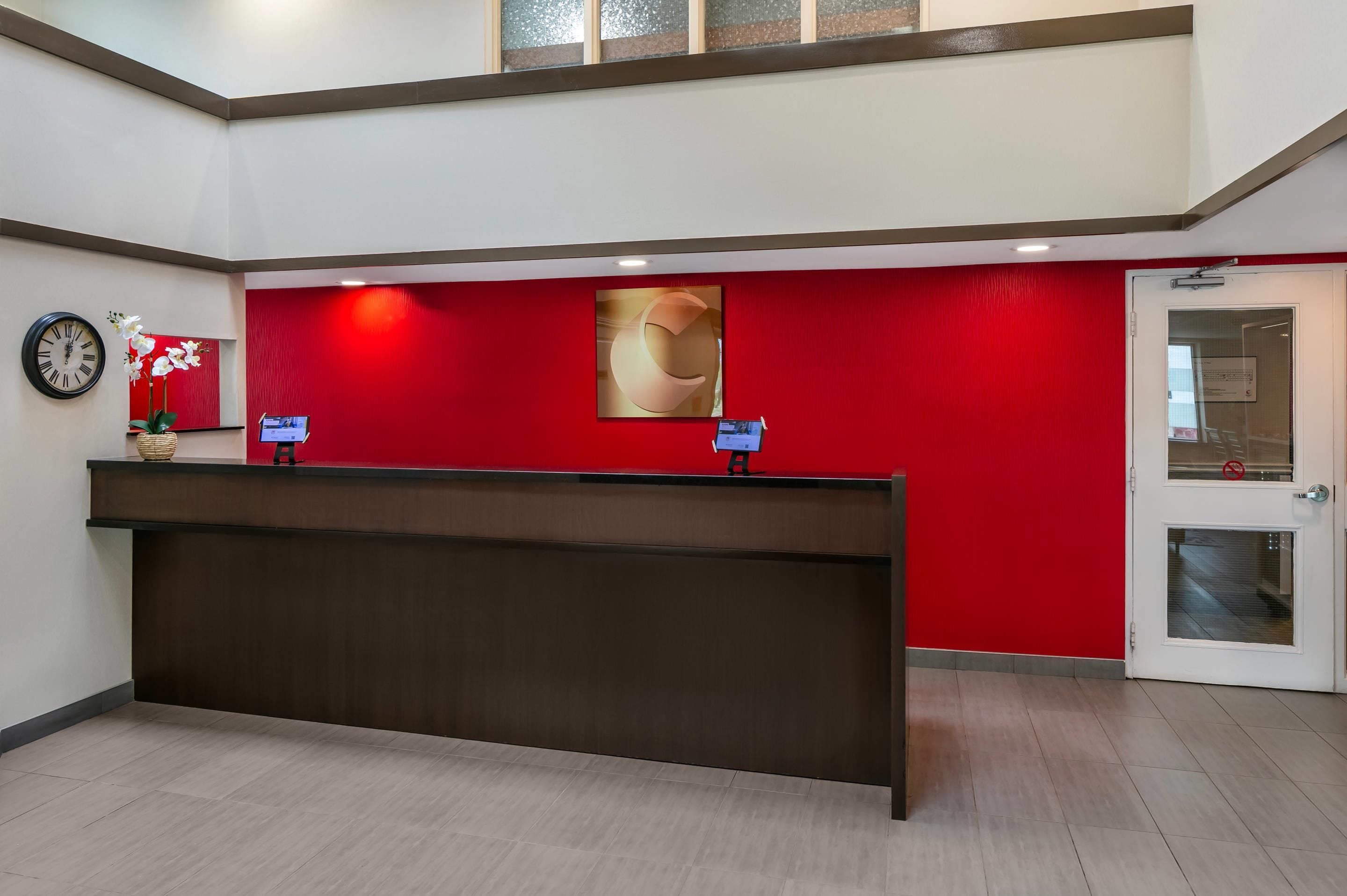 A reception desk with a red wall, a clock, and a flower vase.