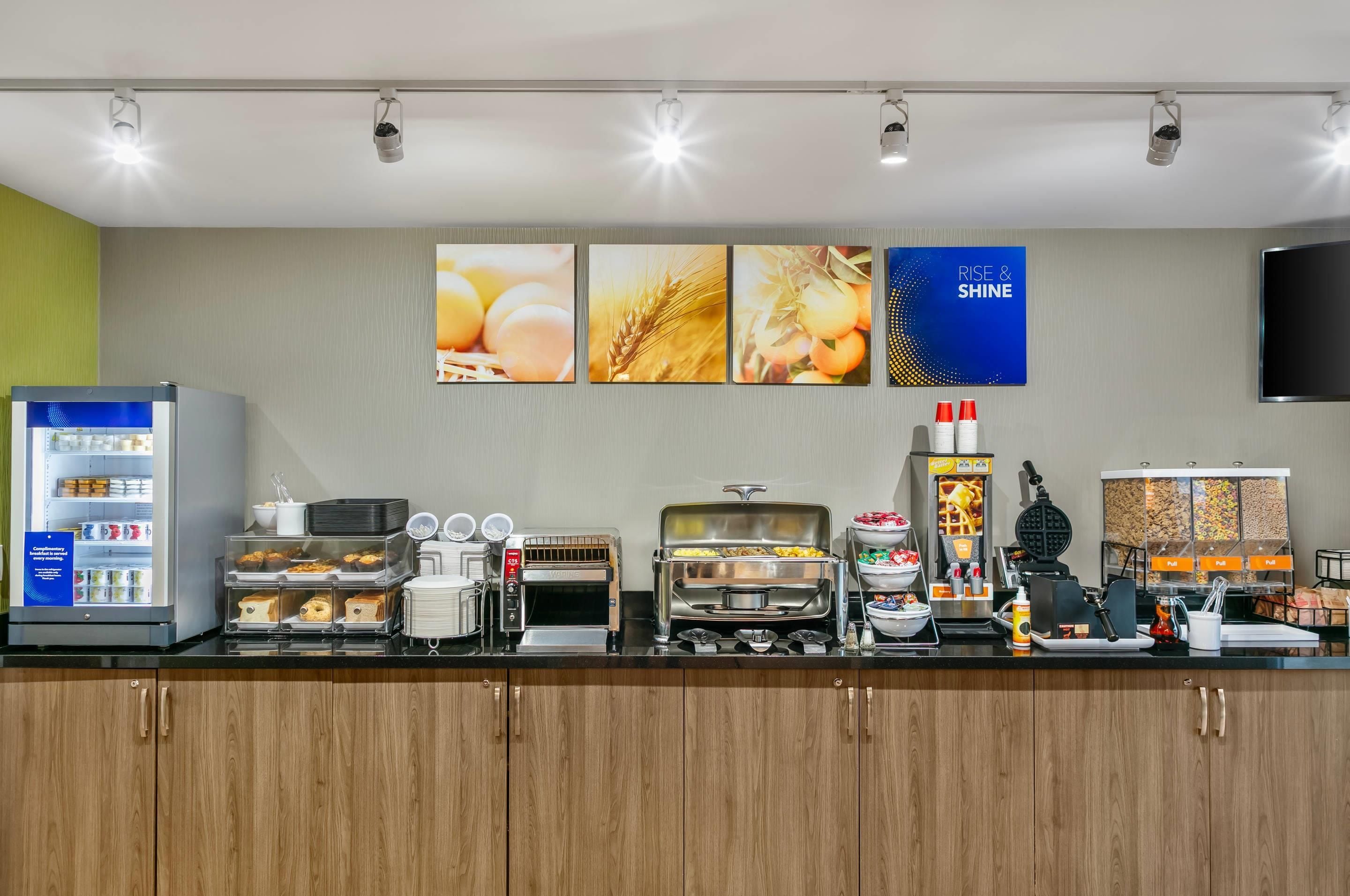 Una barra de desayuno equipada con refrigerador, tostadora, máquina para waffles y diferentes recipientes de comida.