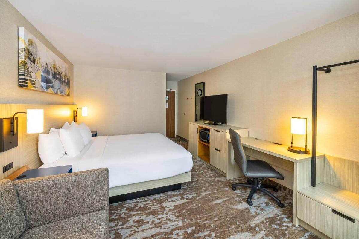 A hotel room with a bed, a desk, a chair, a television, and a painting on the wall.