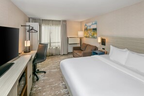 Una habitación de hotel con cama, escritorio y silla, televisión, sofá y un cuadro en la pared.
