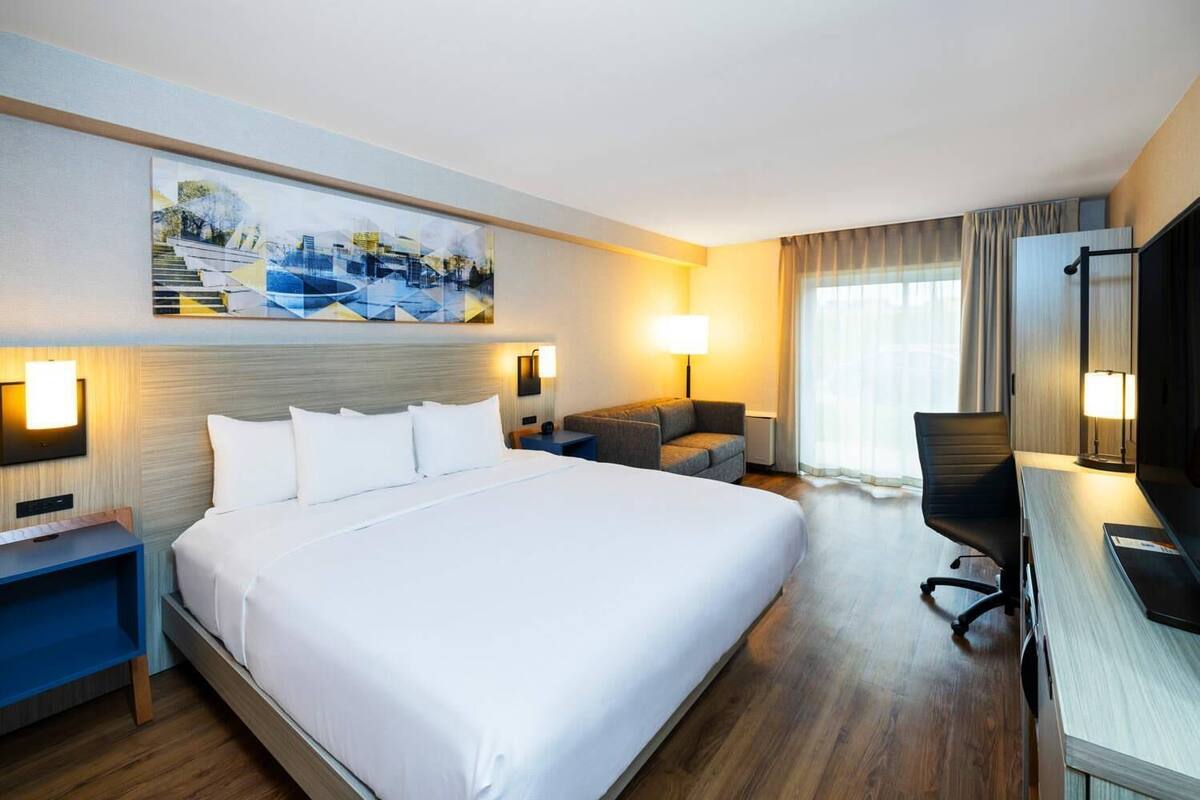 A hotel room with a large bed, a desk, a chair, a sofa, and a painting on the wall.