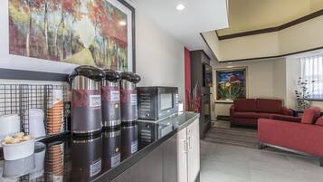 A modern kitchen with coffee dispensers, a microwave, and a red sofa in the living area.