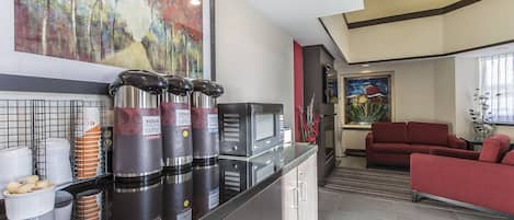 A modern kitchen with coffee dispensers, a microwave, and a red sofa in the living area.