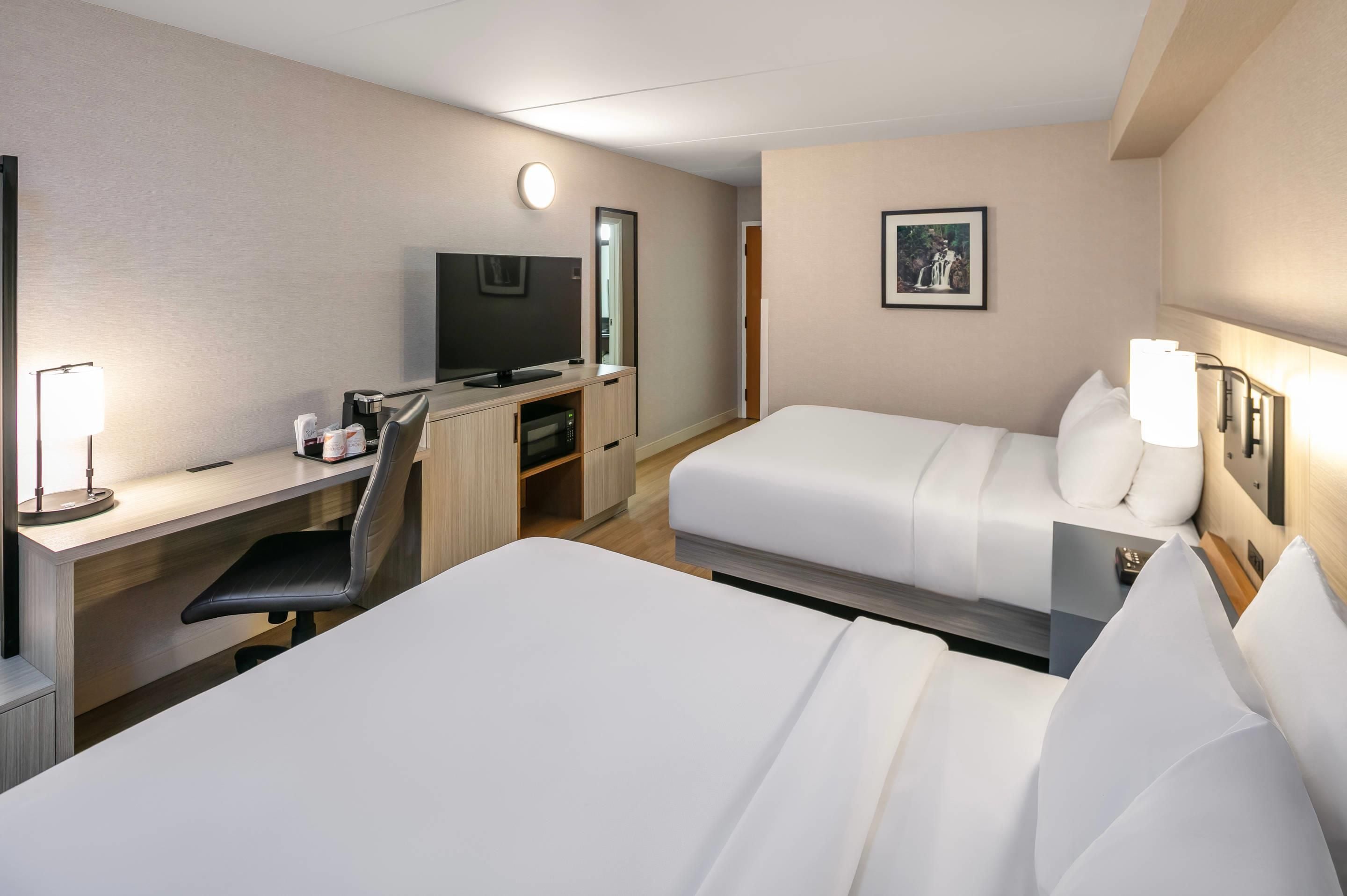 Habitación de hotel con cama, escritorio, silla, televisión y un cuadro en la pared.