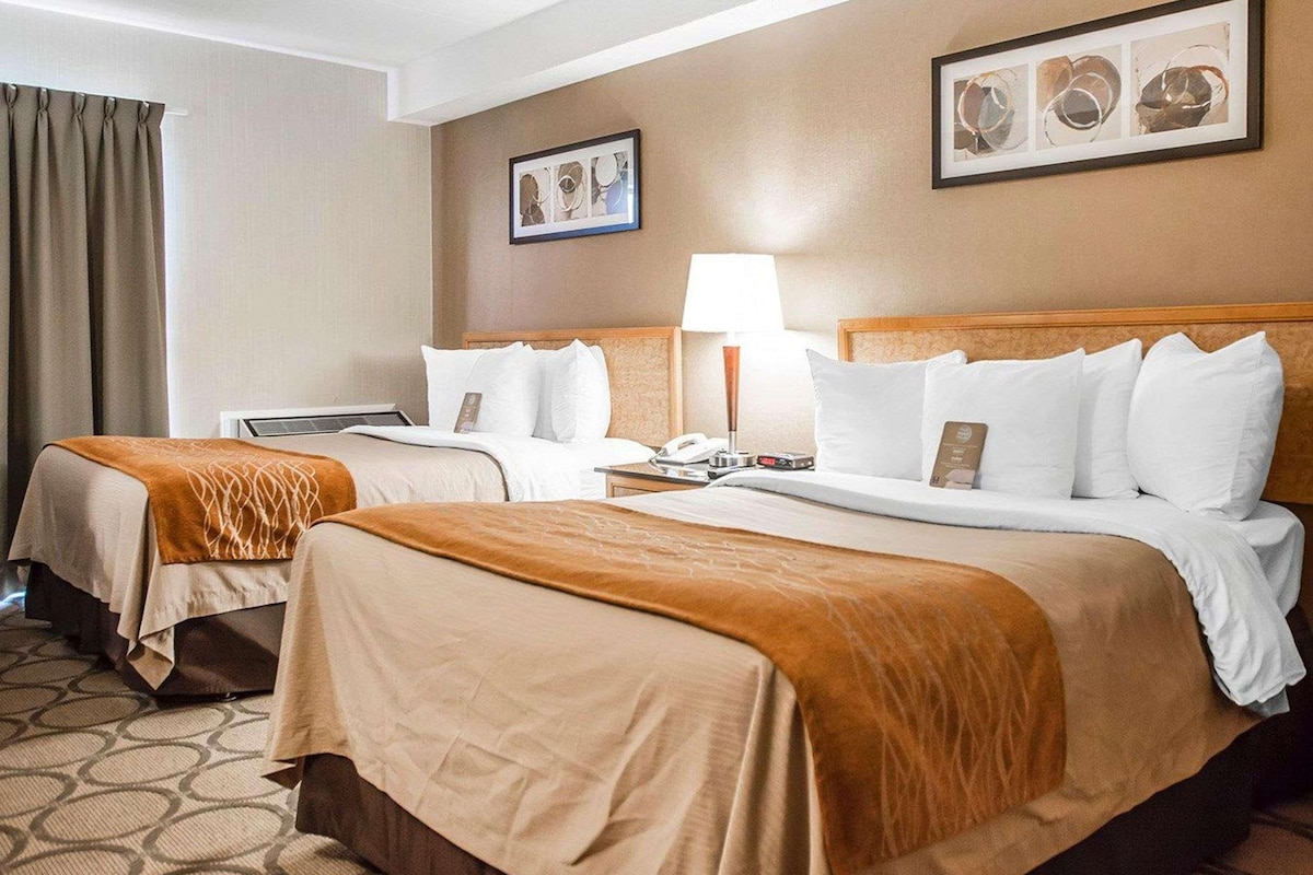 A hotel room with two beds, a desk, a lamp, and artwork on the walls.