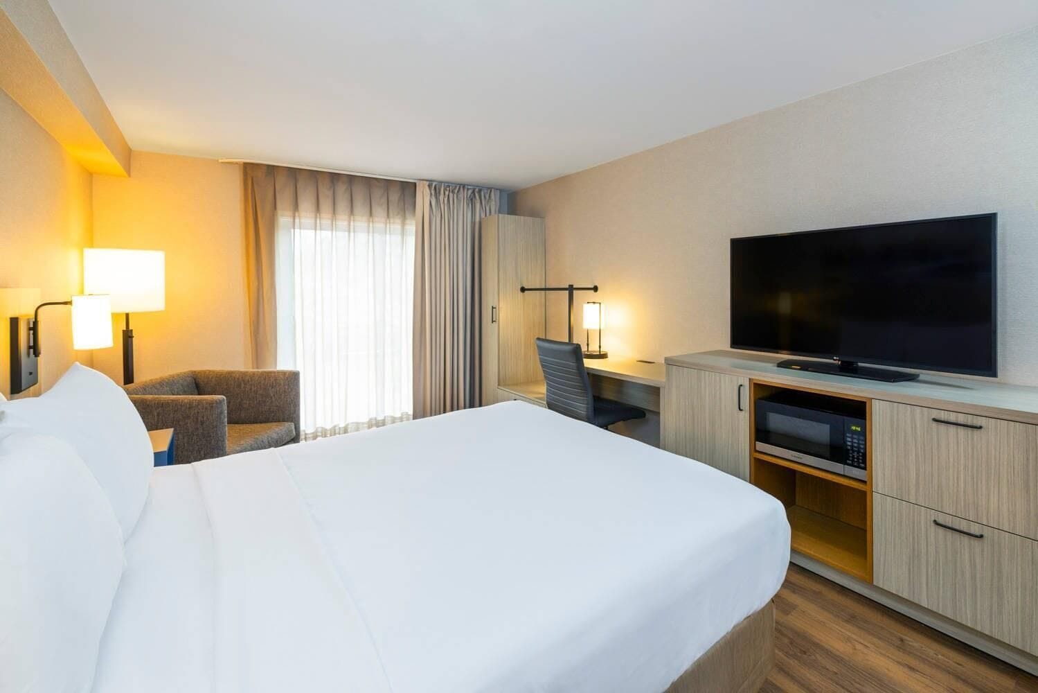 A hotel room with a large bed, a desk with a chair, a television, and a minibar.