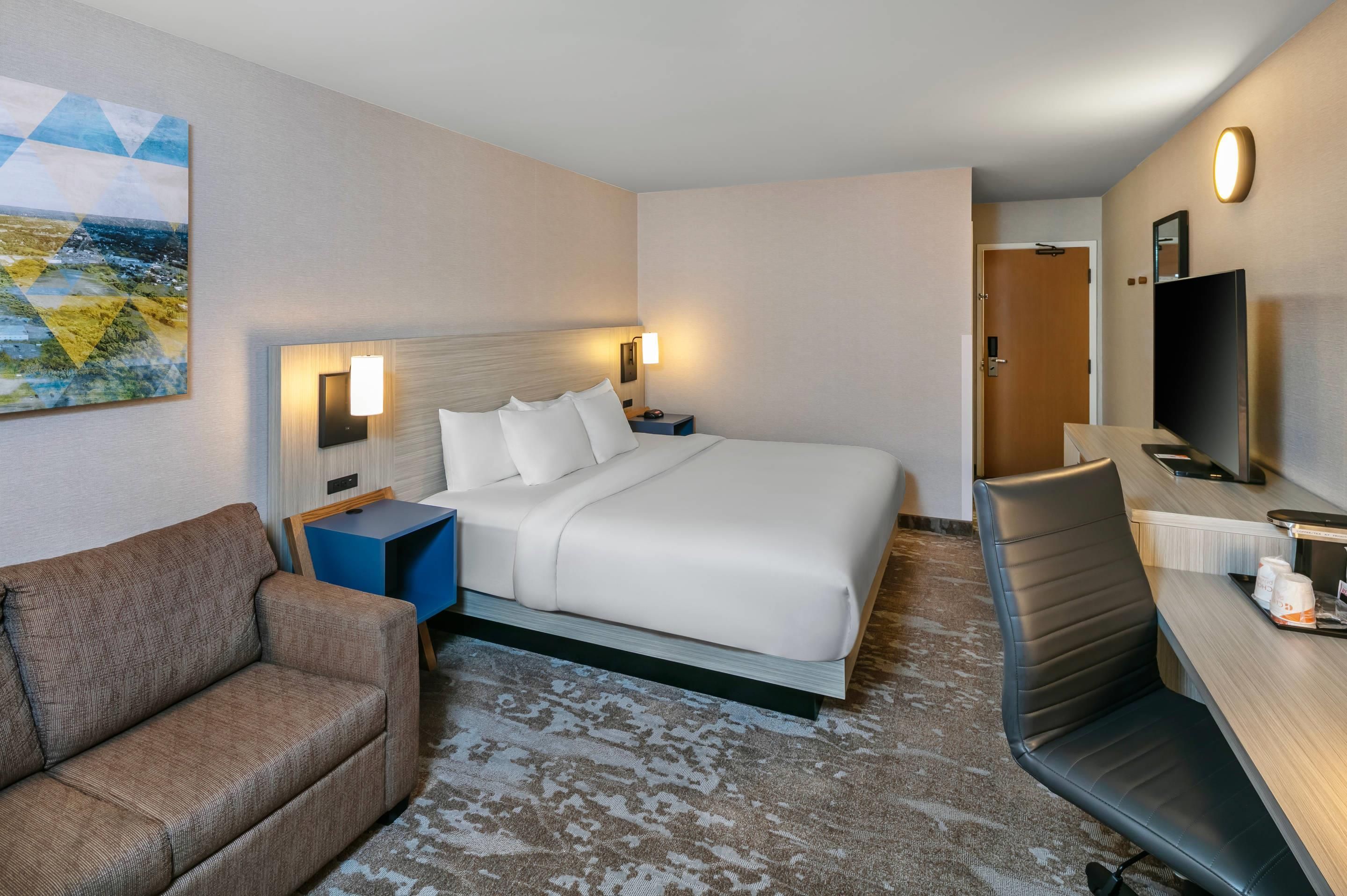 Ein Hotelzimmer mit Bett, Schreibtisch, Stuhl, einer Couch und einem Bild an der Wand.