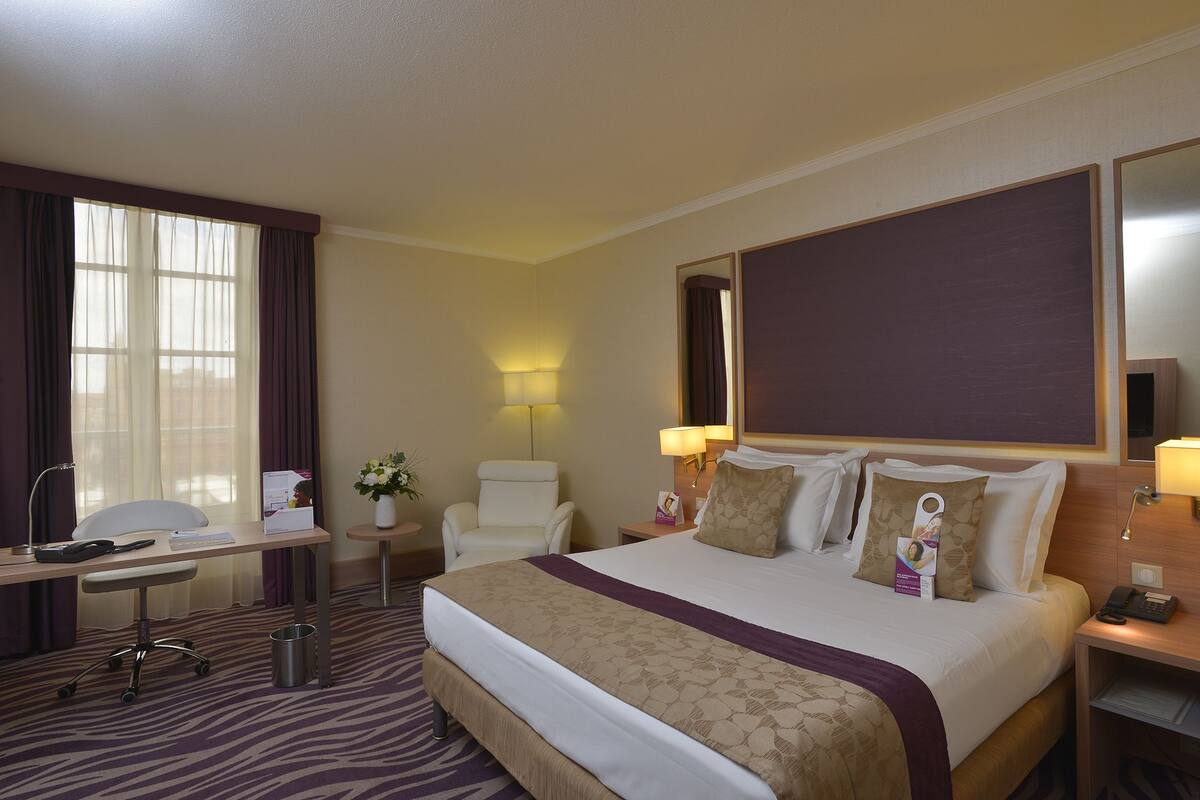 A hotel room with a bed, desk, chair, and a large mirror.