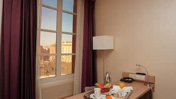 A hotel room with a dining table set with breakfast, a lamp, and a view of a cityscape.
