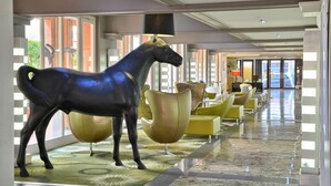 Un vestíbulo de hotel con una gran estatua de un caballo, sillas amarillas modernas y un suelo con estampado de cuadros.