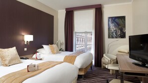 Una habitación de hotel con dos camas, televisión, escritorio y vistas al balcón exterior.