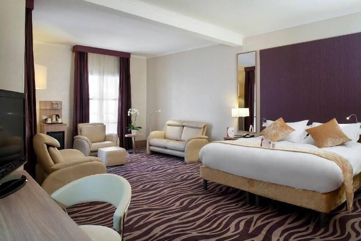 A hotel room with a large bed, a sofa, a chair, a TV, and a desk.
