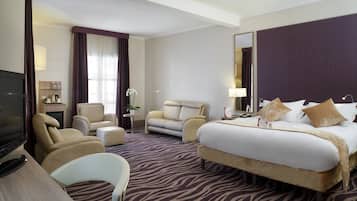 Quarto de hotel com uma cama grande, um sofá, uma escrivaninha com televisão e uma pequena mesa com abajur.