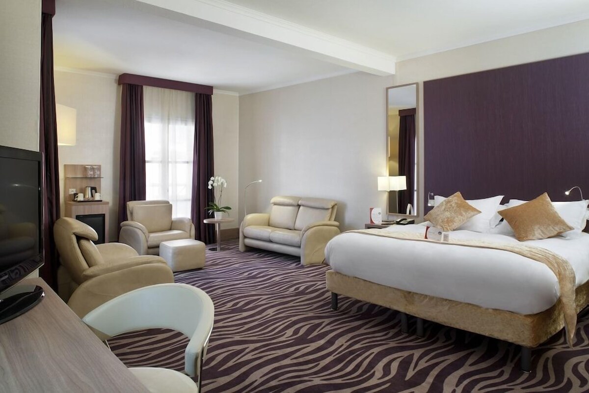 Una camera d'albergo con un letto, due poltrone, un divano, una televisione e una scrivania.