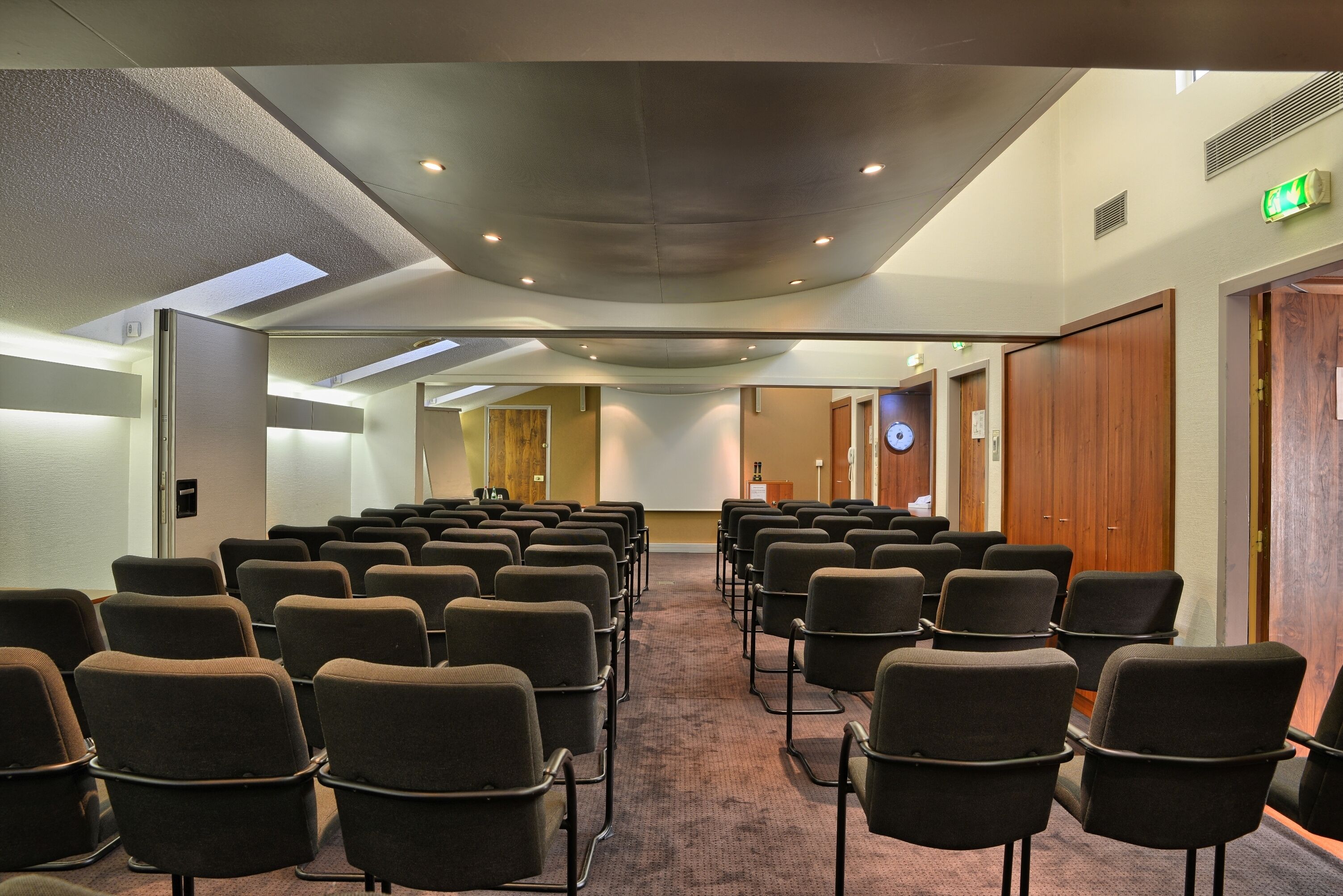 A conference room with rows of chairs, a carpeted floor, and a high ceiling with recessed lighting.