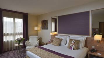 Una habitación de hotel con una cama grande, una silla, una mesita pequeña y una mesita de noche.