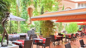 Un patio exterior con sillas y mesas de mimbre, algunas con sombrillas.