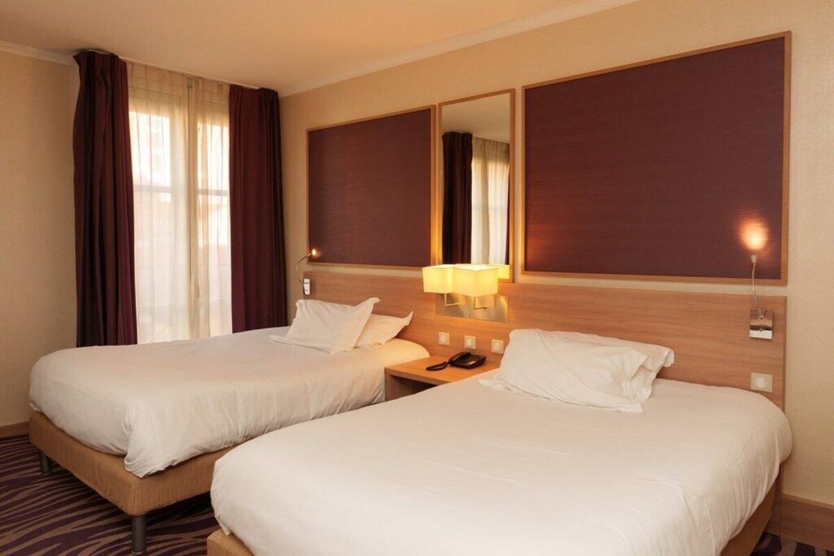A hotel room with two beds, a nightstand with a lamp, a telephone, and a mirror on the wall.