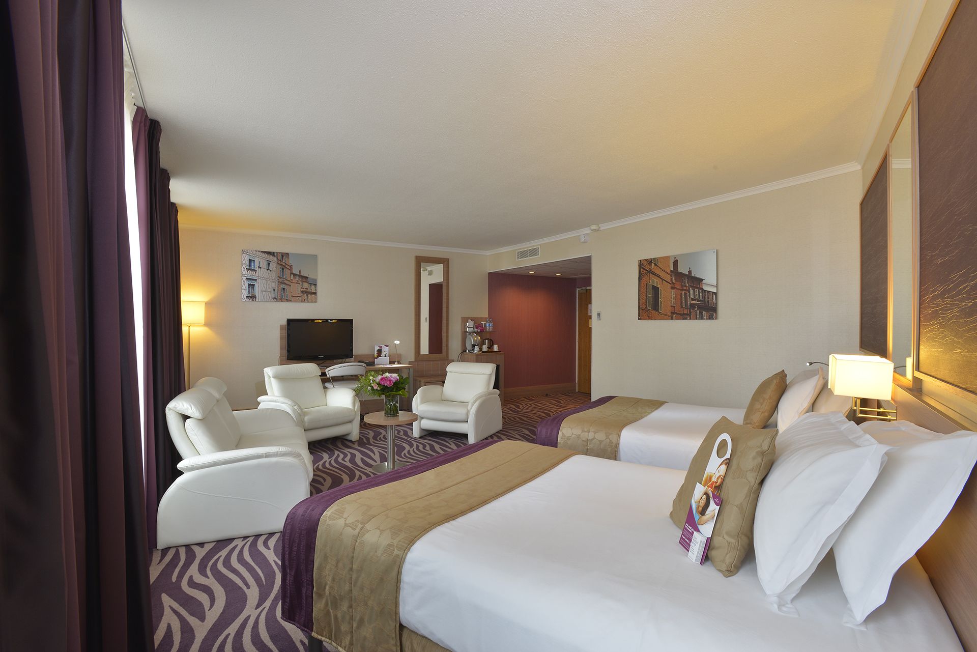 A hotel room with two beds, a sofa, a TV, and a desk.