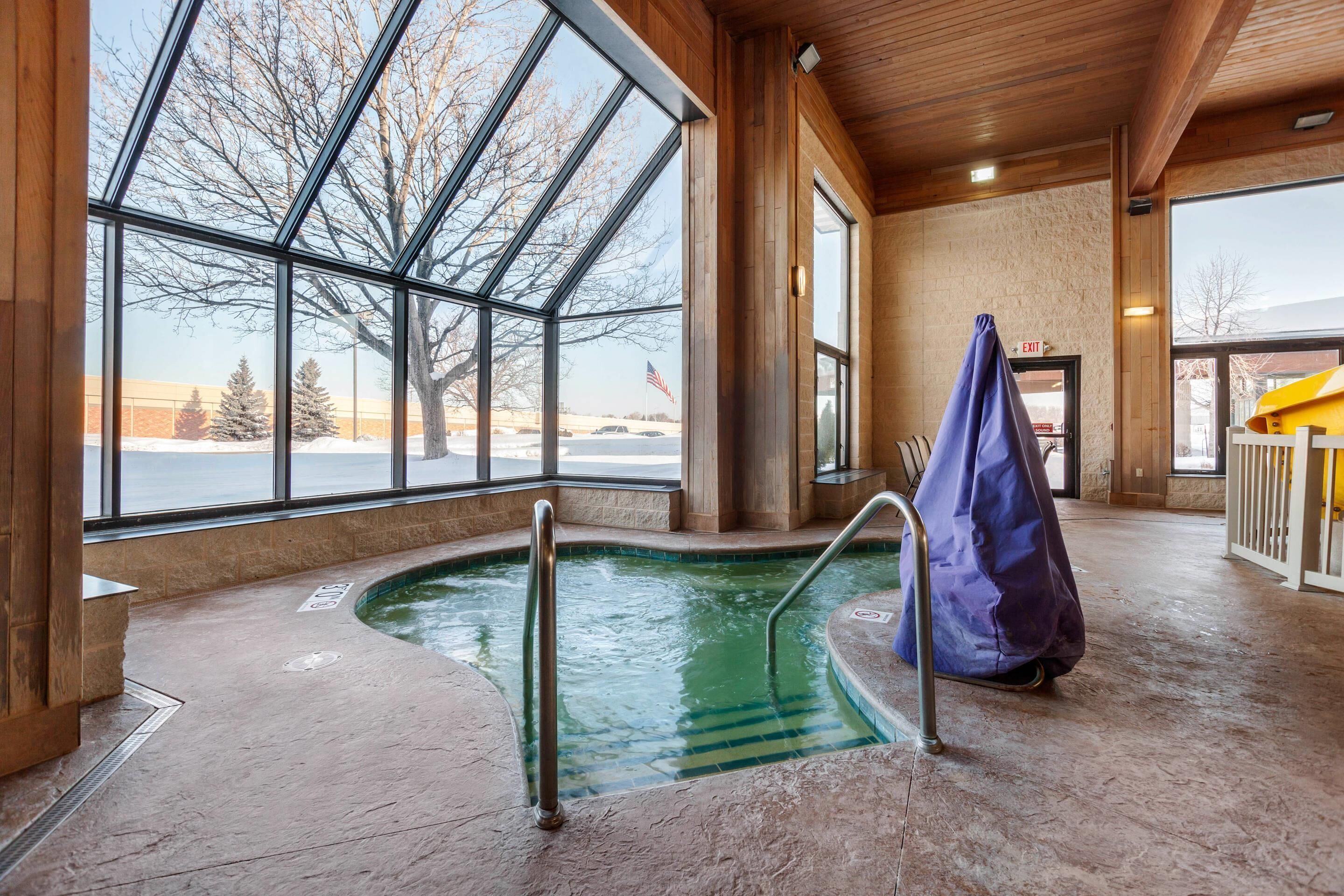 Uma grande piscina interior com paredes de vidro transparente, teto de madeira e vista para uma paisagem nevada.