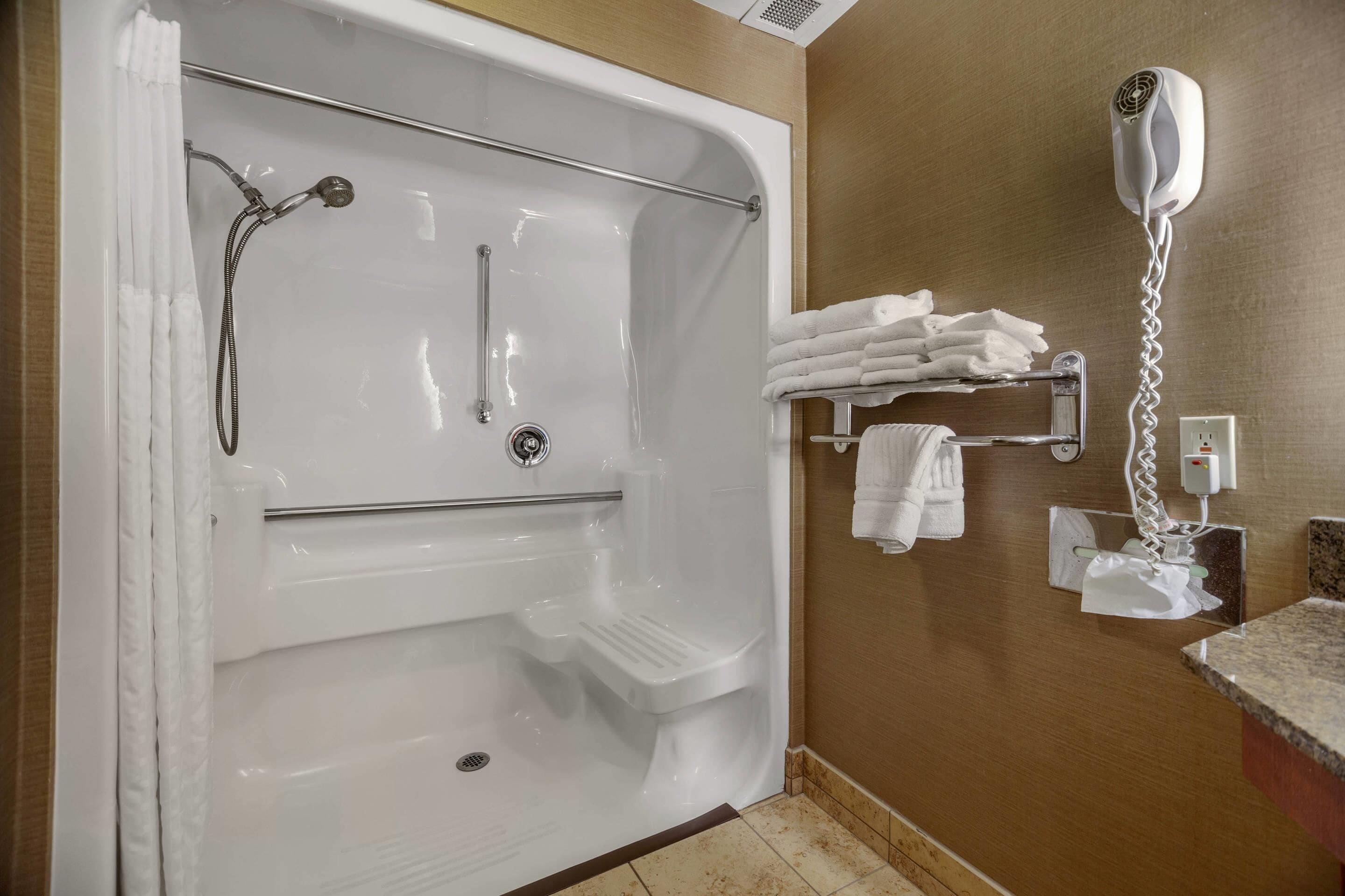A bathroom with a bathtub, a shower, a towel rack with towels, and a hairdryer on the wall.