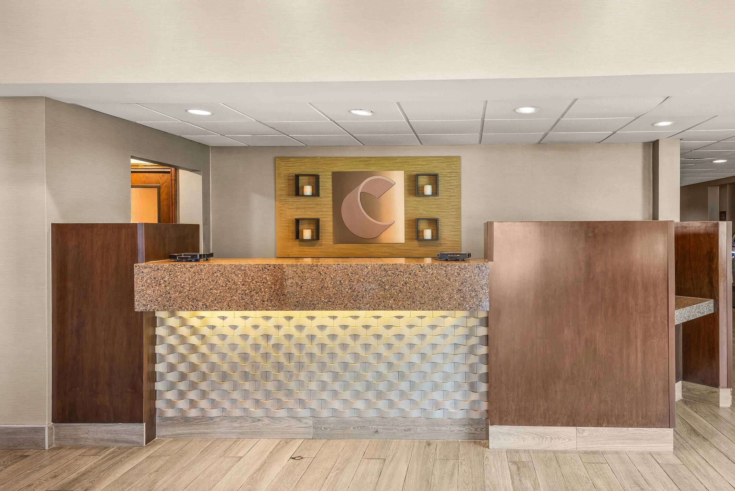 A reception desk with a wooden finish, a patterned wall behind it, and a ceiling with recessed lighting.