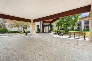 A covered outdoor area with a concrete floor, a building entrance, and benches.