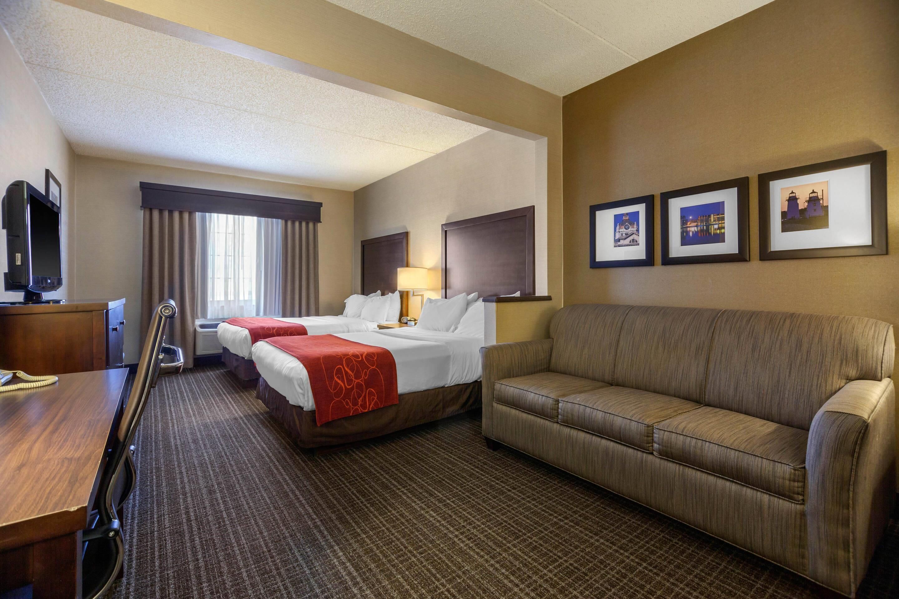 A hotel room with two beds, a sofa, a TV, and framed pictures on the wall.