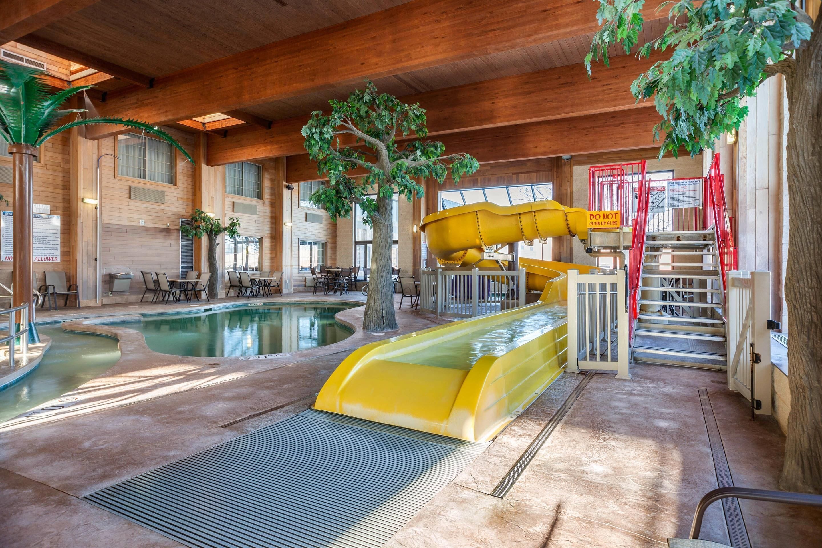 An indoor pool area with a slide, seating, and a tree.