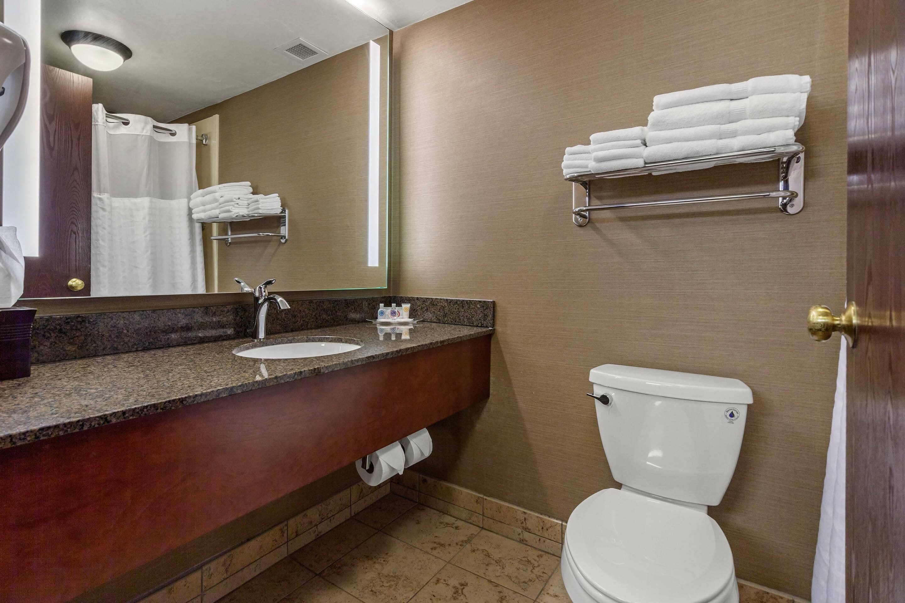 Ein Badezimmer mit Waschbecken, Spiegel, Handtuchhalter, Toilette und Handtuchspender.