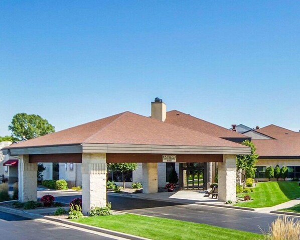 A hotel with a covered outdoor area, a sign indicating a caution for low clearance, and a well-maintained lawn.