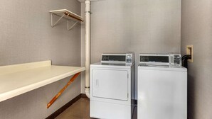 Ett tvättrum med två tvättmaskiner och två torktumlare placerade ovanpå varandra, ett träställ för torkning och en vit hylla.