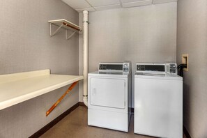 A laundry room with two stacked washers and dryers, a wooden drying rack, and a white shelf.