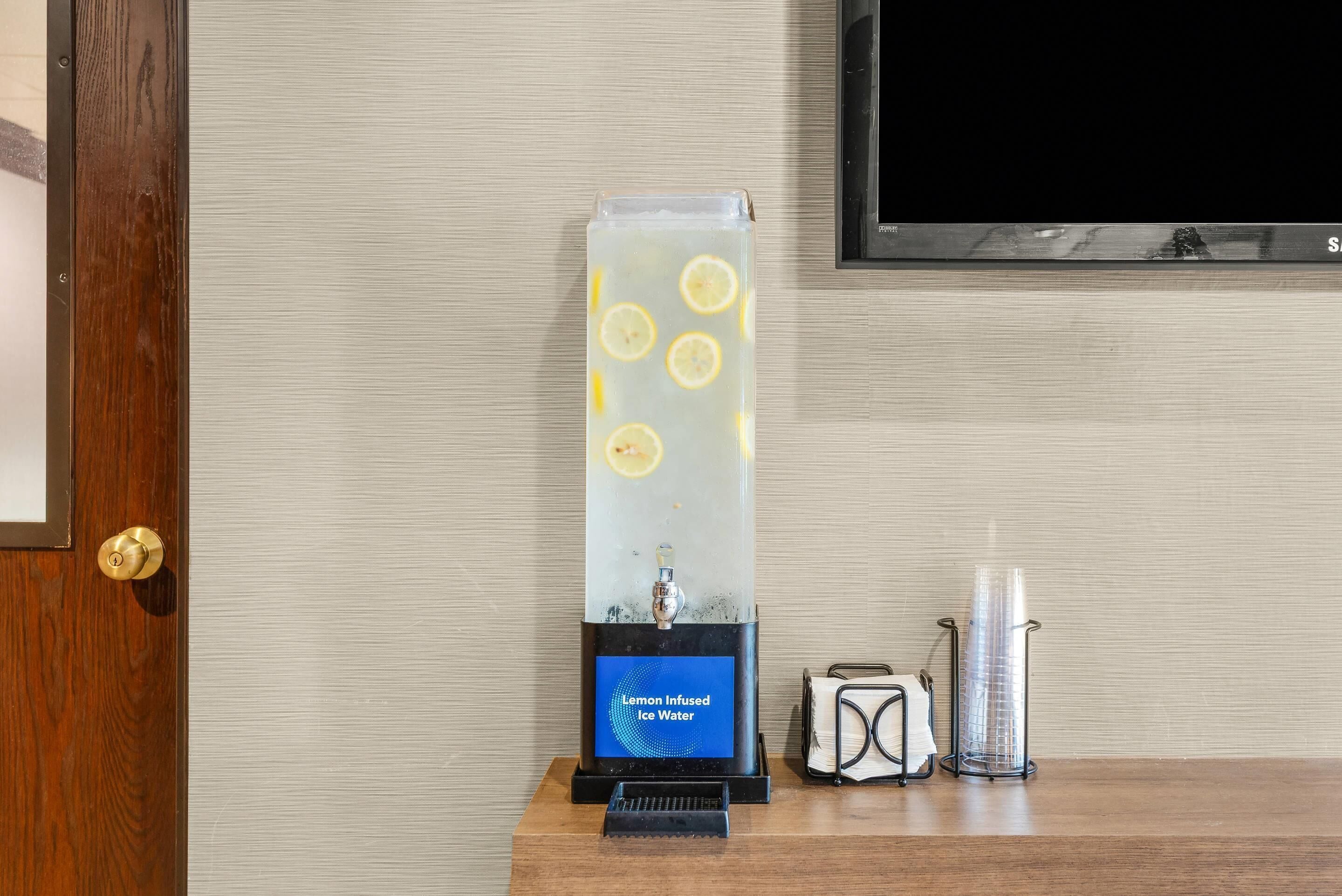 Een verticale dispenser met een digitaal scherm waarop staat 'Lemon Infused Ice Water' en een glazen vat met citroenpartjes.
