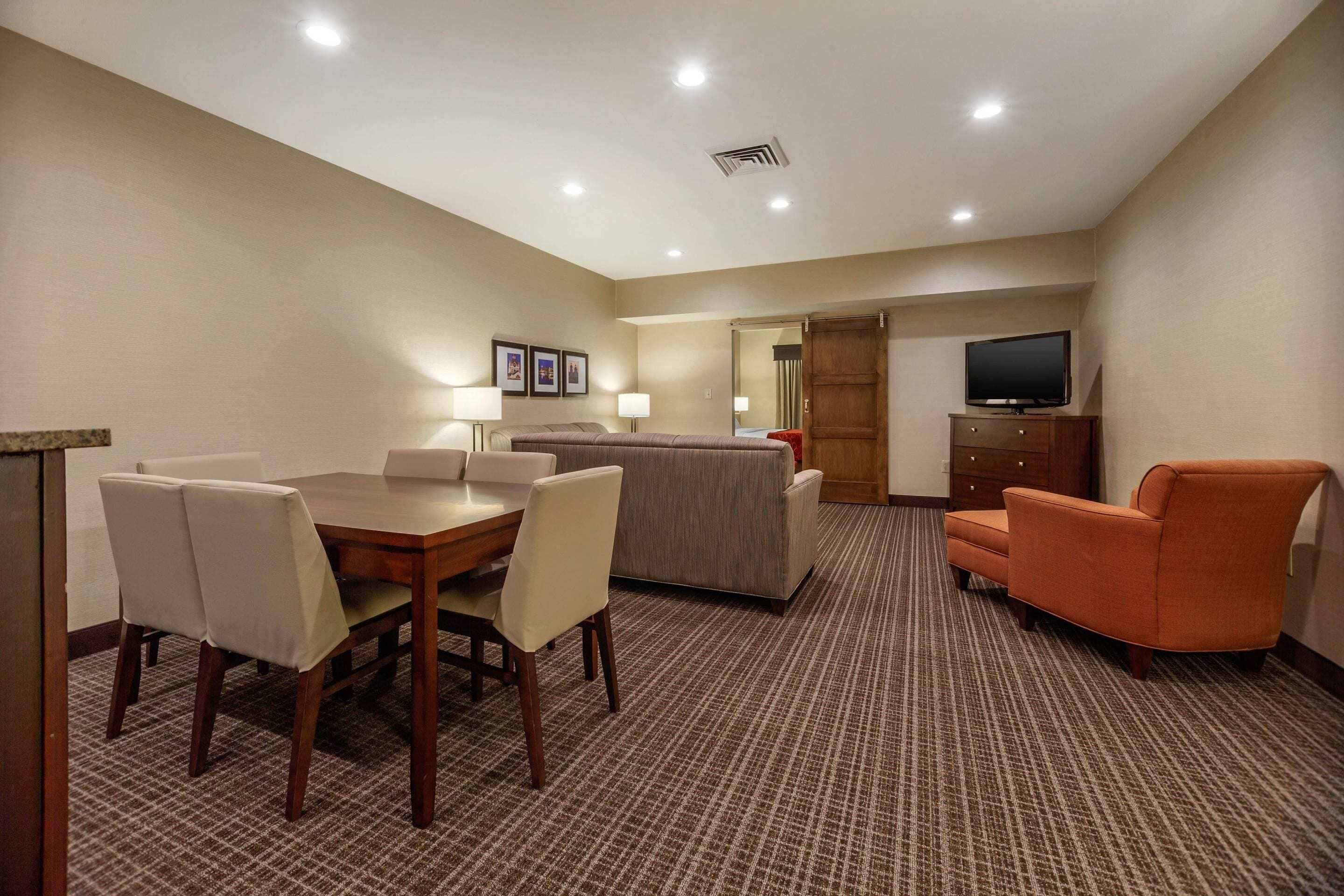 A hotel room with a dining table, chairs, a sofa, a television, and a cabinet.