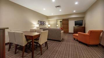 A hotel room with a dining table, chairs, a sofa, a television, and a cabinet.