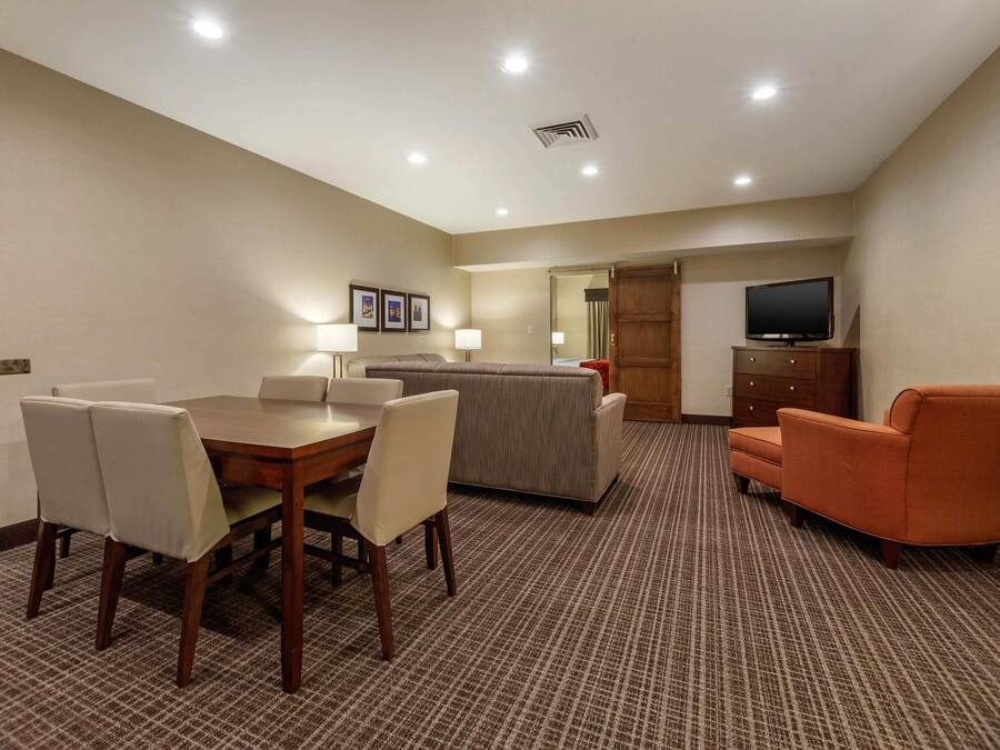 A hotel room with a dining table, chairs, a sofa, a television, and a cabinet.