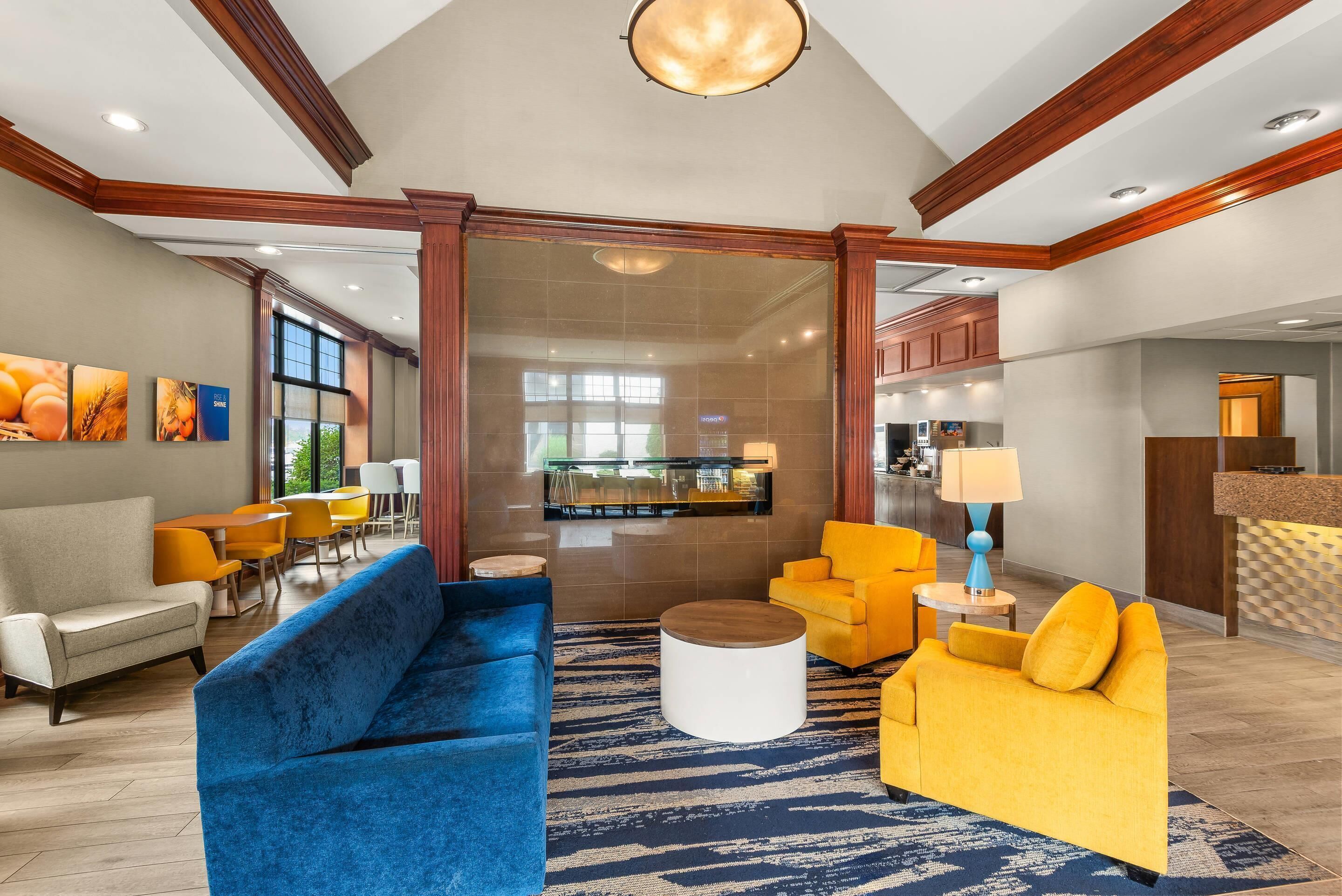 A hotel lobby with a blue sofa, yellow armchairs, a reception desk, and a large window.