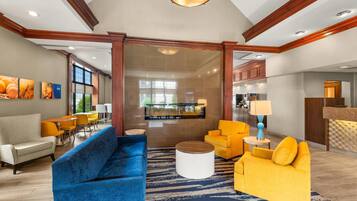 A hotel lobby with a blue sofa, yellow armchairs, a reception desk, and a large window.