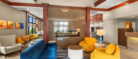 A hotel lobby with a blue sofa, yellow armchairs, a reception desk, and a large window.