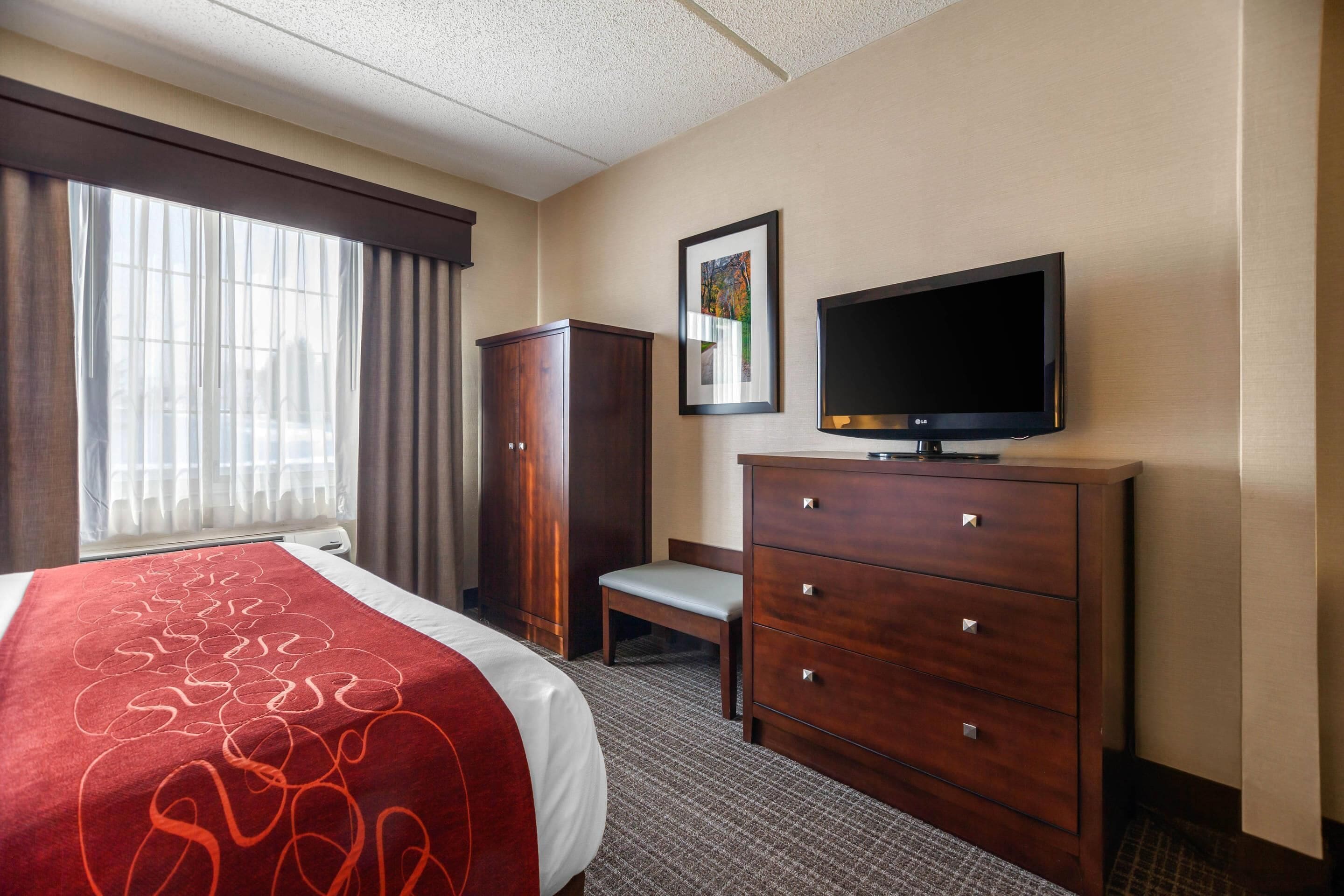 Een hotelkamer met een bed, een televisie op een houten dressoir, een bureau en een raam met gordijnen.